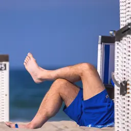 Ein Mann liegt zwischen Strandkörben am Strand.